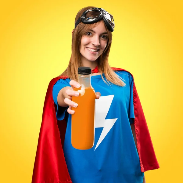 Pretty superhero girl holding a orange juice on colorful backgro