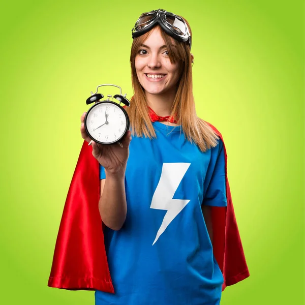 Hübsches Superheldenmädchen hält Vintage-Uhr auf buntem Hintergrund — Stockfoto
