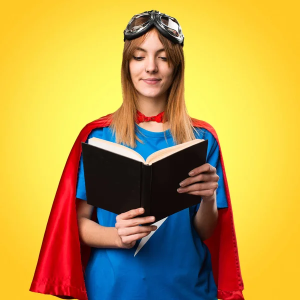 Pretty superhero girl reading book on colorful background