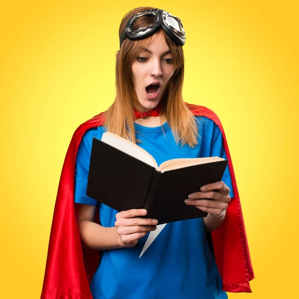 Pretty superhero girl reading book on colorful background