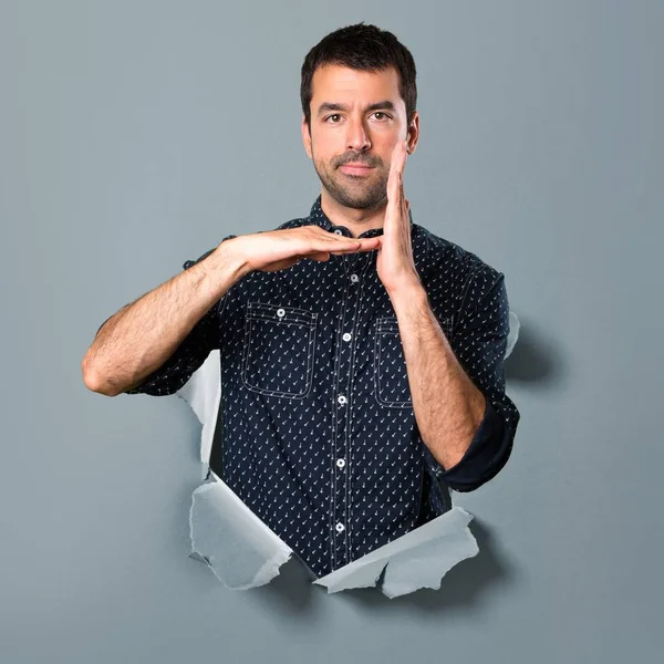 Morena hombre haciendo tiempo fuera gesto a través de un agujero de papel —  Fotos de Stock
