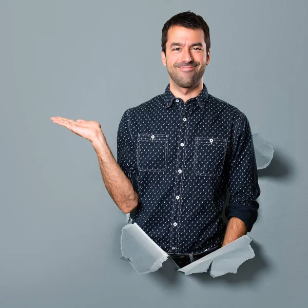 Brunette man holding something through a paper hole