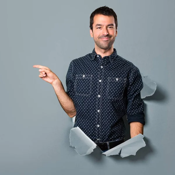 Morena hombre apuntando hacia el lateral a través de un agujero de papel —  Fotos de Stock