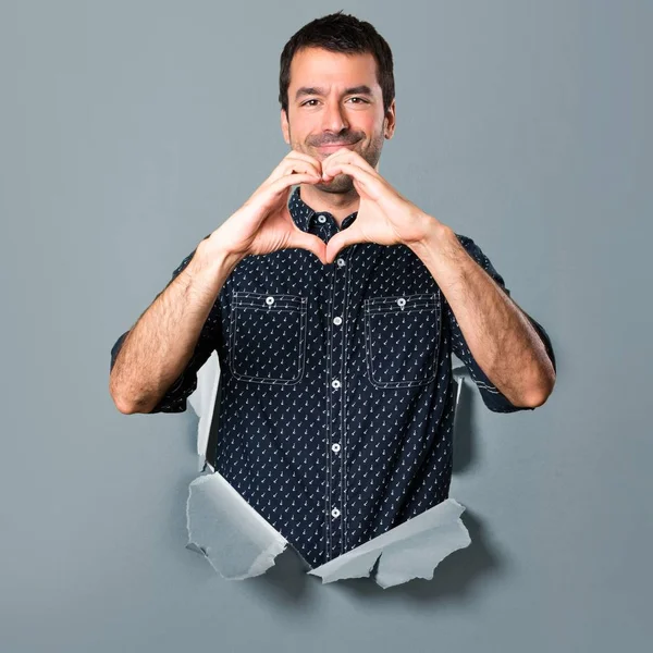 Morena hombre haciendo un corazón con las manos a través de un agujero de papel — Foto de Stock