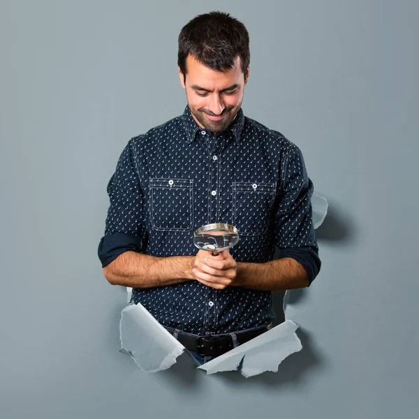 Brunett man med förstoringsglas genom ett papper hål — Stockfoto