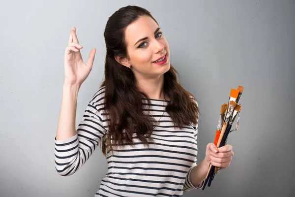 Jonge kunstenaar vrouw met haar vingers oversteken op grijze achtergrond — Stockfoto