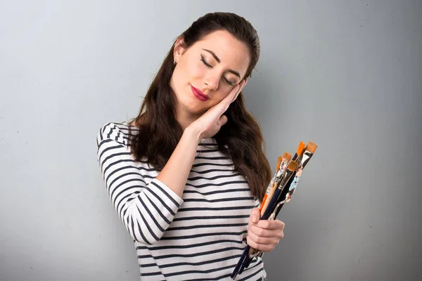 Junge Künstlerin macht Schlafgeste auf grauem Hintergrund — Stockfoto