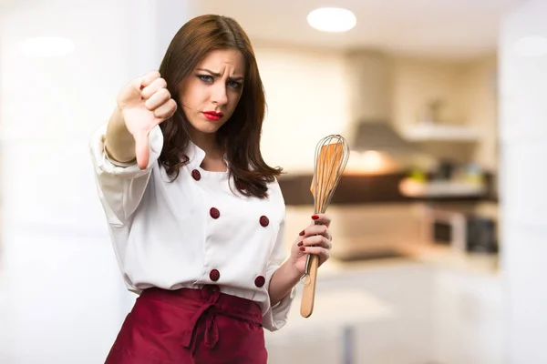 Beautiful chef woman making bad signal on unfocused background