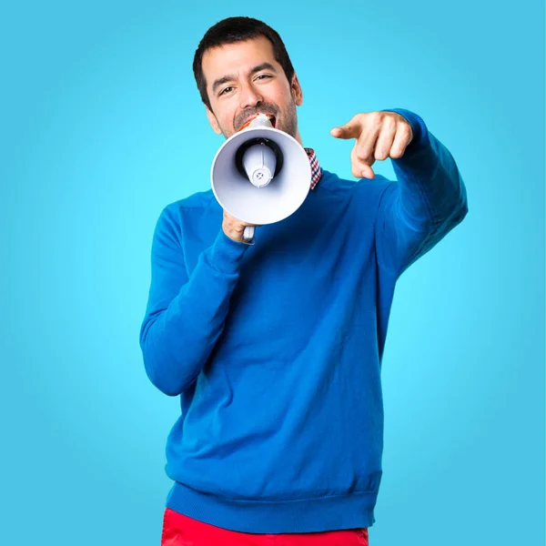 Guapo joven sosteniendo un megáfono sobre fondo colorido — Foto de Stock
