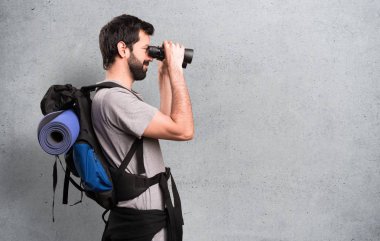 Mutlu yakışıklı backpacker dokulu arka plan üzerinde dürbün ile