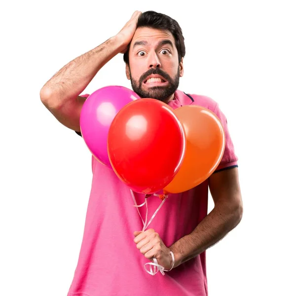 Απογοητευμένοι όμορφος νεαρός άνδρας κρατώντας μπαλόνια πάνω από απομονωμένες λευκό φόντο — Φωτογραφία Αρχείου