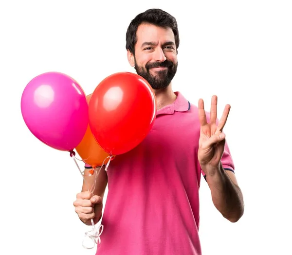 英俊的年轻人持有气球和计数三在孤立的白色背景 — 图库照片