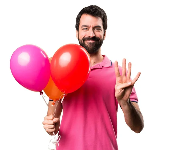 Handsome young man holding balloons counting four over isolated white background — Stock Photo, Image