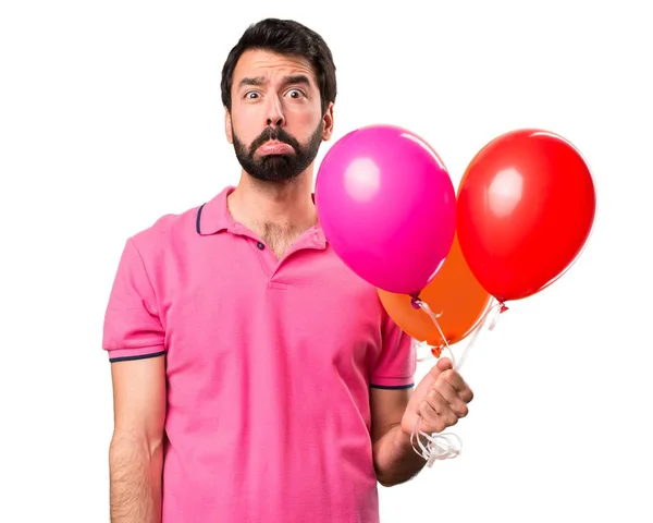 Θλιβερή όμορφος νεαρός άνδρας κρατώντας μπαλόνια πάνω από απομονωμένες λευκό φόντο — Φωτογραφία Αρχείου