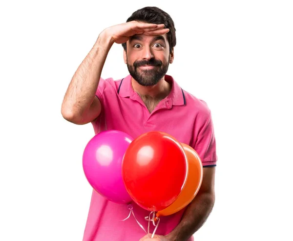 Όμορφος νεαρός άνδρας κρατά μπαλόνια και δείχνει κάτι πέρα από το απομονωμένο λευκό φόντο — Φωτογραφία Αρχείου