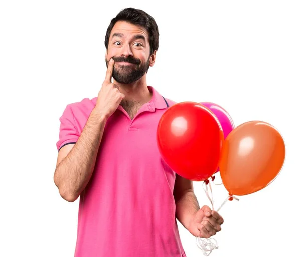 Ευτυχισμένος όμορφος νεαρός άνδρας κρατώντας μπαλόνια πάνω από απομονωμένες λευκό φόντο — Φωτογραφία Αρχείου