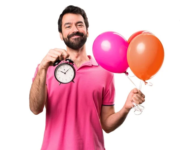 Bello giovane uomo che tiene palloncini e tiene orologio vintage su sfondo bianco isolato — Foto Stock
