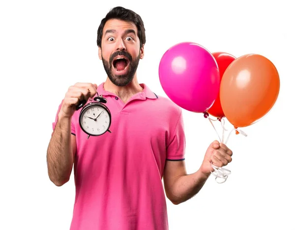 Handsome young man holding balloons and  holding vintage clock over isolated white background — Stock Photo, Image