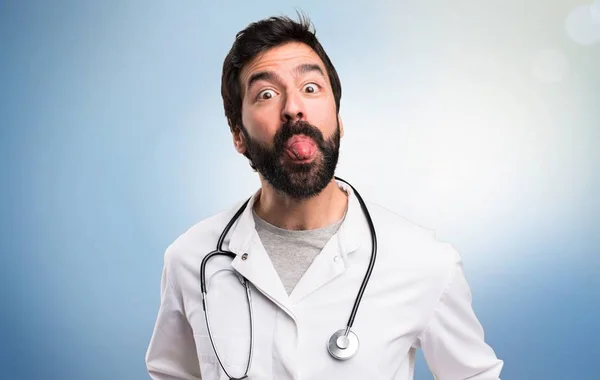Jeune médecin sortant sa langue sur fond bleu — Photo