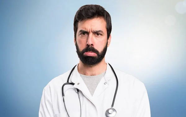 Trauriger junger Arzt auf blauem Hintergrund — Stockfoto