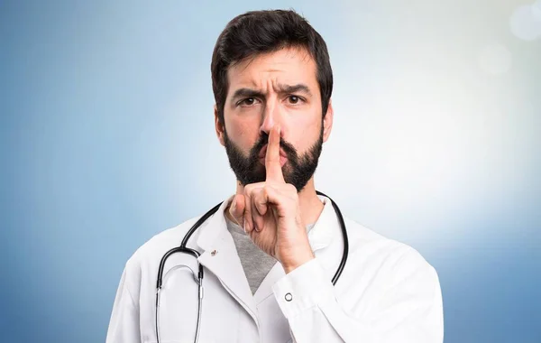 Young doctor making silence gesture on blue background — Stock Photo, Image