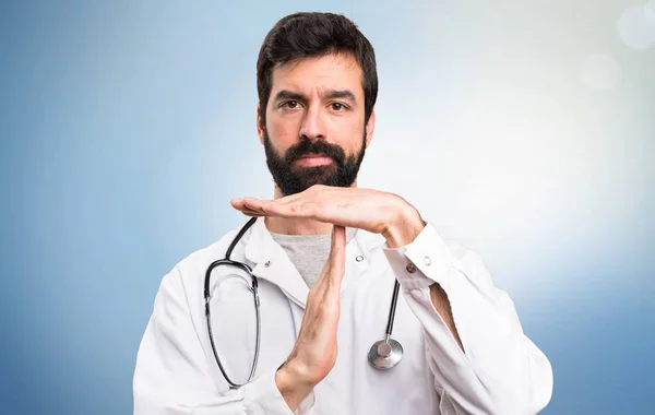 Young doctor making time out gesture on blue background — Stock Photo, Image