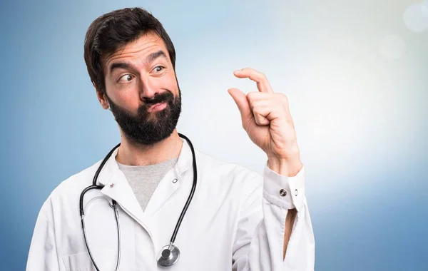 Joven médico haciendo minúscula señal sobre fondo azul — Foto de Stock