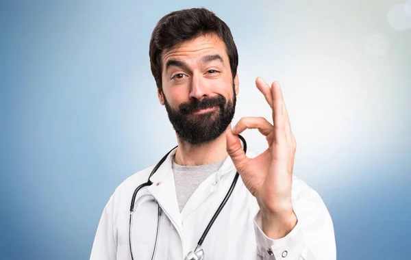 Young doctor making OK sign on blue background — Stock Photo, Image