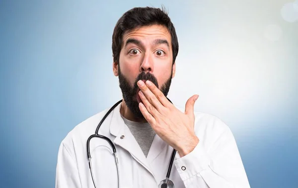 Joven médico haciendo gesto sorpresa sobre fondo azul — Foto de Stock