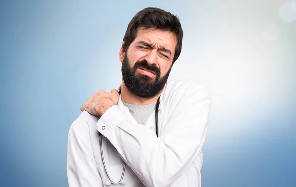 Jovem médico com dor no ombro em fundo azul — Fotografia de Stock