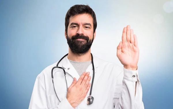 Joven médico haciendo un juramento sobre fondo azul — Foto de Stock