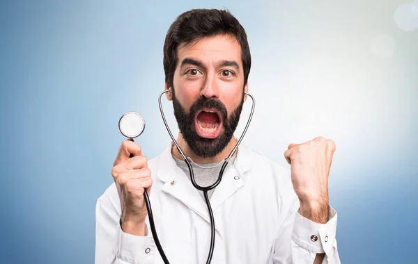 Médico joven con estetoscopio sobre fondo azul —  Fotos de Stock