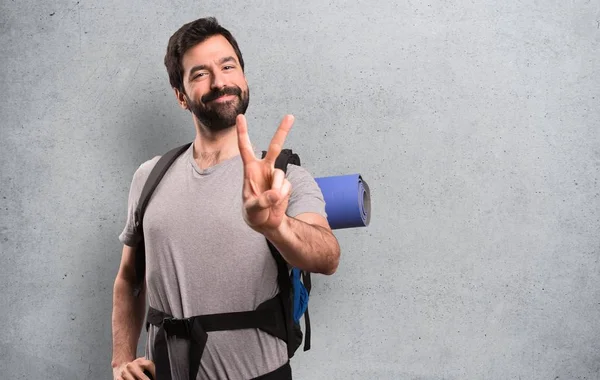 Handsome backpacker making victory gesture on textured background — Stock Photo, Image