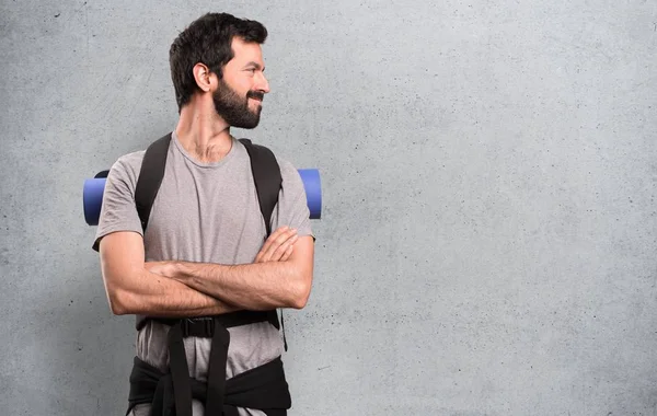 Yakışıklı backpacker dokulu arka plan üzerinde yanal arıyorsunuz — Stok fotoğraf
