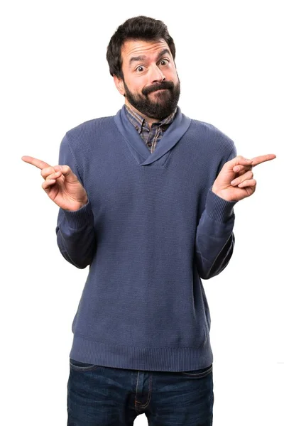 Handsome brunette man with beard pointing to the laterals having doubts on white background — Stock Photo, Image