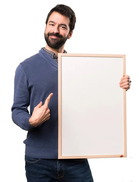 Feliz Bonito morena homem com barba segurando um cartaz vazio no fundo branco — Fotografia de Stock