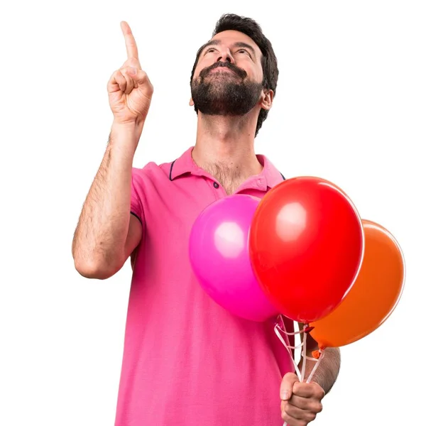 Handsome young man holding balloons and  pointing up over isolated white background — Stock Photo, Image