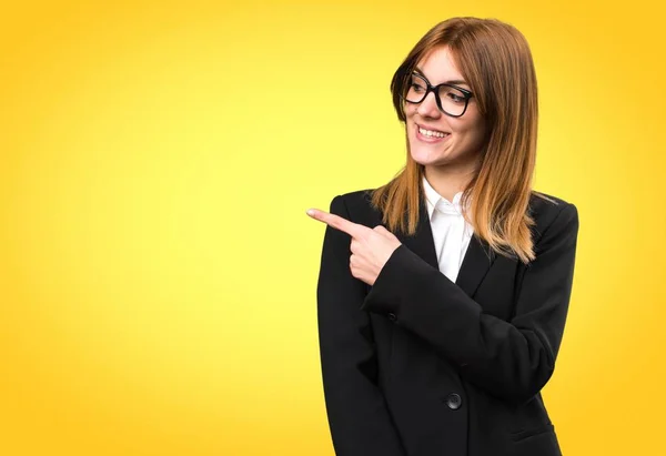 Young business woman pointing to the lateral on colorful background — Stock Photo, Image