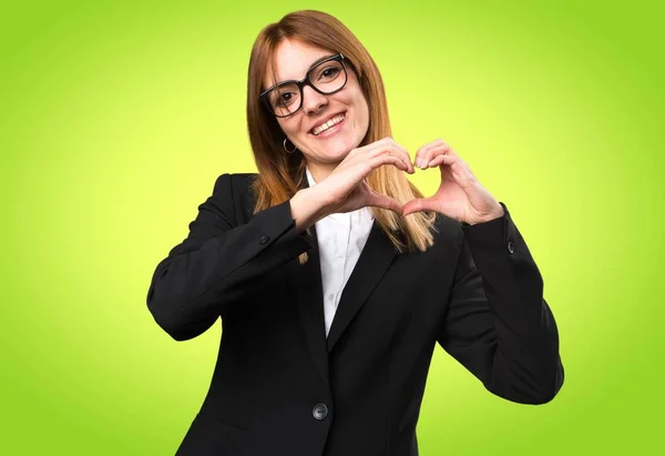 Jovem mulher de negócios fazendo um coração com as mãos no fundo colorido — Fotografia de Stock