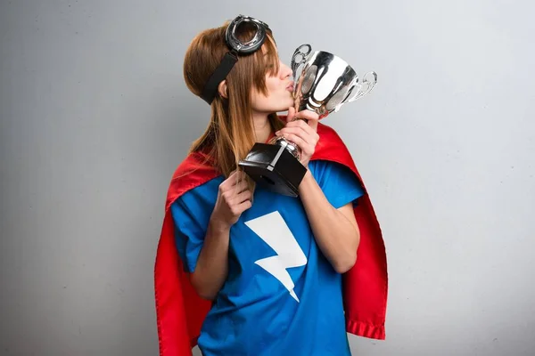 Menina super-herói bonito segurando um troféu em um fundo texturizado cinza — Fotografia de Stock