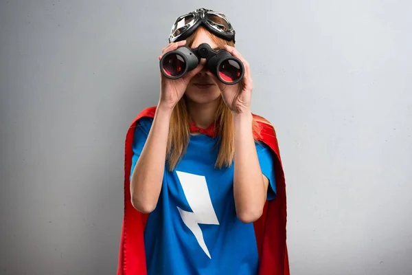 Pretty superhero girl with binoculars on a gray textured background — Stock Photo, Image