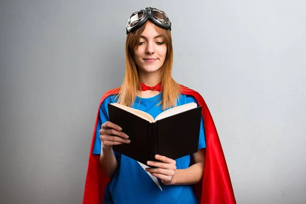 Pretty superhero girl reading book on a gray textured background