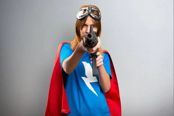 Pretty superhero girl holding a rifle on a gray textured background — Stock Photo, Image