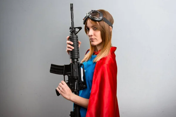 Bella ragazza supereroe in possesso di un fucile su uno sfondo grigio strutturato — Foto Stock