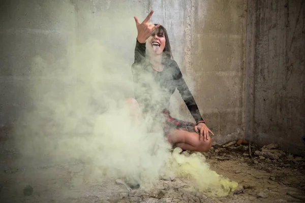 Hermosa joven con bomba de humo en un edificio abandonado haciendo gesto de roca — Foto de Stock