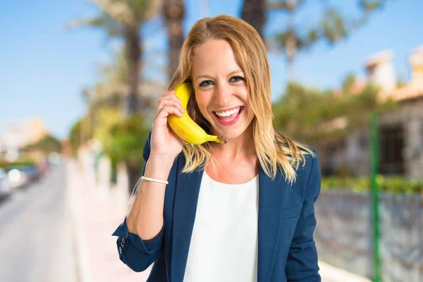 Menina loira com banana como telefone sobre fundo branco — Fotografia de Stock