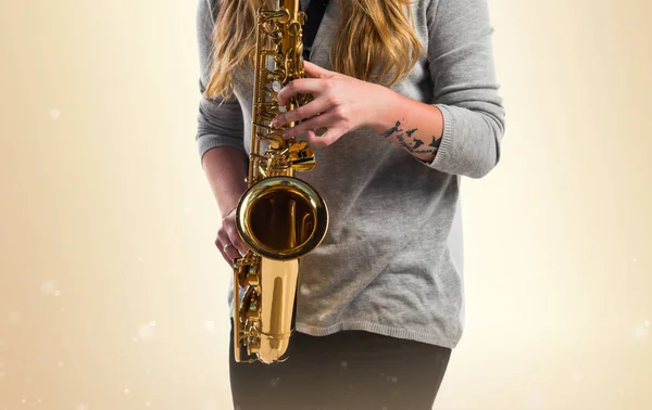 Dívka hraje na saxofon na okrové pozadí — Stock fotografie