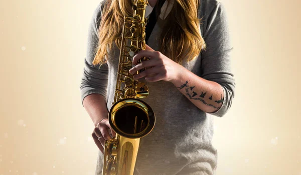 Dívka hraje na saxofon na okrové pozadí — Stock fotografie