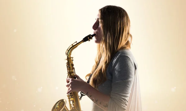 Chica tocando el saxofón sobre fondo ocre —  Fotos de Stock