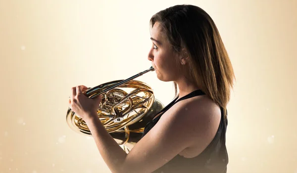 Girl playing the french horn on ocher background — Stock Photo, Image
